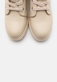 Sneaker in pelle beige con punte arrotondate, lacci piatti e occhielli in metallo; superficie testurizzata con finitura liscia; suole in gomma.
