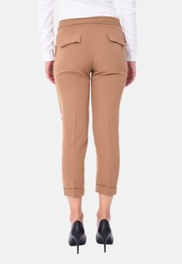 Pantaloni cropped beige con una texture liscia, dotati di tasche posteriori e risvolti, abbinati a scarpe con tacco nere.