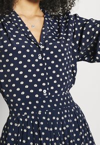 Marindräkt med vitt cirkulärt mönster, knäppning framtill, krage och plisserad kjol. Mjuk tygkvalitet, avslappnad passform och trekvartsärmar.