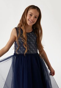 Navy blue dress featuring a patterned bodice with sparkle accents and a layered tulle skirt. Sleeveless design with a gathered waist.