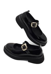 Schwarze Lackleder-Mary-Jane-Schuhe mit runder Zehenpartie, verstellbarem Schnallenriemen und einer stabilen schwarzen Gummisohle mit strukturierten Kanten.