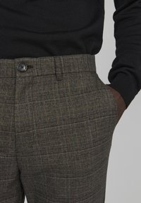 Mörka rutiga byxor i nyanser av grått och brunt, med en framficka, knappstängning och slät textur.