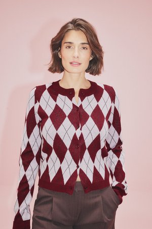 Bordeaux en witte argyle-patroon cardigan, met knoopsluiting aan de voorkant, ronde hals, lange mouwen, zachte breistekstuur. Draagt het met een paar bruine broeken.