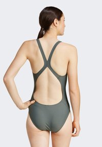 Maillot de bain une pièce vert foncé, avec un design à dos nageur et une découpe ouverte à l'arrière. Fabriqué en matériau lisse et extensible.
