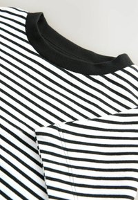 Gros plan sur une chemise à rayures noir et blanche, avec un col noir et une poche visible, mettant en valeur le tissu et les détails de couture.