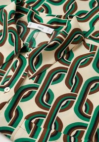 Chemise à manches courtes en tissu léger avec un fond beige orné d'un motif en chaîne de couleurs verte, marron et noire, fermée par des boutons.