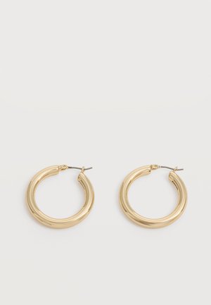 Paire de boucles d'oreilles épaisses en or brillant avec tiges métalliques sur un fond gris clair.