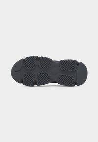 Semelle d'une chaussure de sport noire avec des coussinets de traction épais et segmentés, présentant des motifs en zigzag pour une meilleure adhérence.