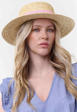 Jeune femme aux longs cheveux blonds portant un chapeau de paille à large bord avec un ruban rose et un haut rayé bleu à col en V.