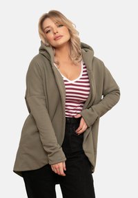 Oliwkowy kardigan z kapturem, z długimi rękawami, luźny krój i przednie kieszenie, nałożony na biały top w burgundowe paski z dekoltem w serek.