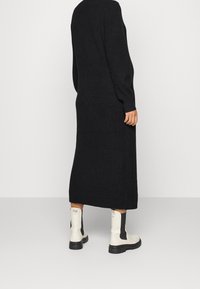 Pitkä musta neulemekko, jossa on ribbineulos ja pitkät hihat, ulottuen keskivarsiin. Yhdistetty valkoisiin nilkkureihin, joissa mustia yksityiskohtia.