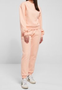 Sweat-shirt en coton couleur pêche et jogging assorti. Le sweat-shirt possède un col rond et des poignets élastiques ; le jogging a une ceinture élastique.