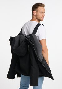 Wasserabweisende schwarze Außenjacke mit grauem Innenfutter und Kapuze, getragen über einem weißen Shirt und hellblauen Jeans. Mit einem Reißverschluss ausgestattet.