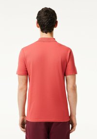 Kortärmad polo i korallfärg, tillverkad av strukturerad tyg. Har en klassisk krage och rak skärning. Inga synliga logotyper eller mönster.