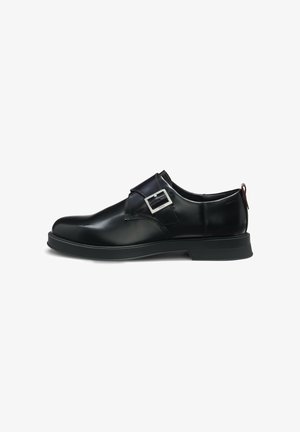 Black leather shoe with a smooth finish, featuring a side buckle detail, rounded toe, and a flat rubber sole.