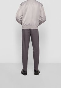 Giacca bomber satin grigia chiara abbinata a pantaloni della tuta grigi scuri. Texture liscia; polsini a costine sulla giacca, pantaloni slim-fit, scarpe nere.