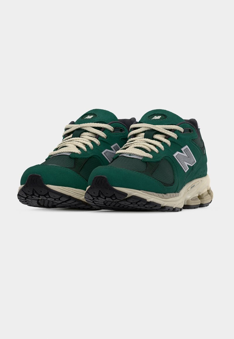 Paire de baskets New Balance vertes et noires avec des lacets blancs et des semelles intermédiaires beige, vues de face sur un fond blanc.