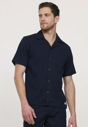 Chemise bleu marine à manches courtes avec boutons, fabriquée en tissu léger. Comprend un col, une poche poitrine unique et une coupe droite.