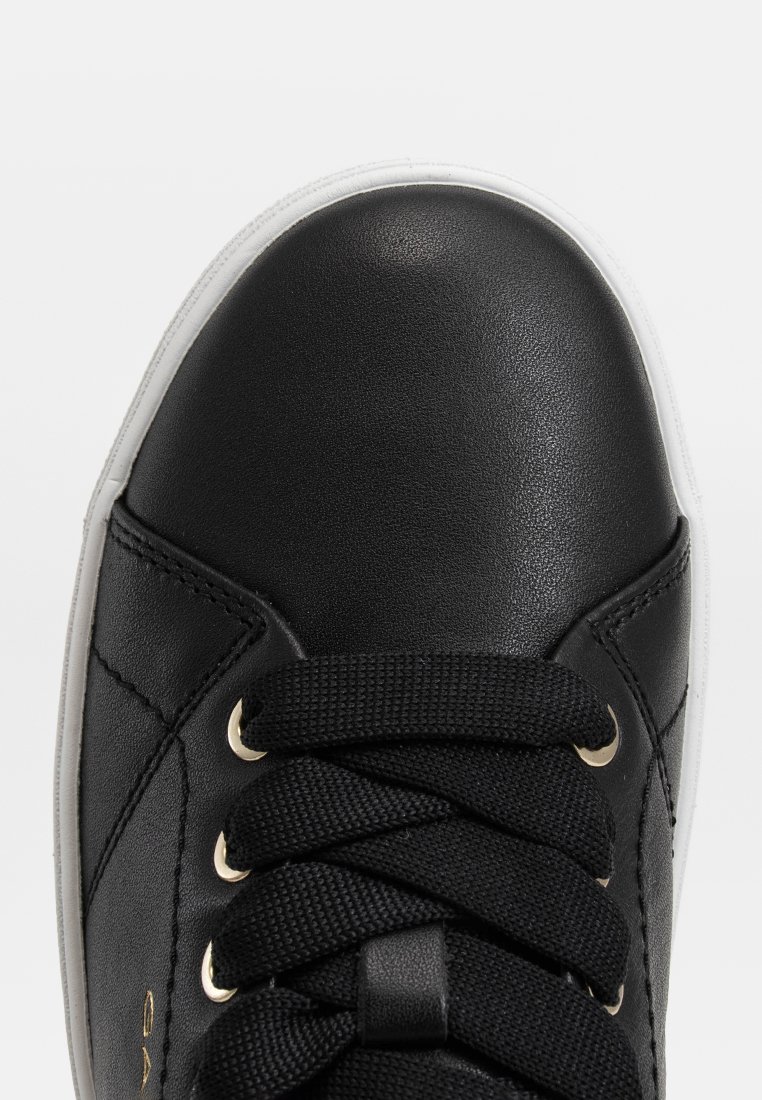 Sneaker in pelle nera con punta arrotondata, dotato di occhielli dorati e lacci neri. La suola è bianca con una superficie texture.