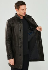 Zwarte leren jas met een staande kraag, voorzien van knoopsluiting, twee zijzakken en een gladde binnenvoering met een zak.