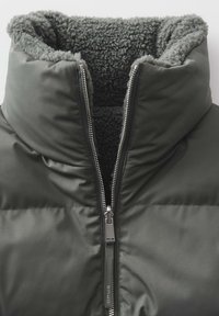 Veste matelassée noire avec doublure sherpa grise, fermeture éclair métallique partiellement ouverte et col montant.