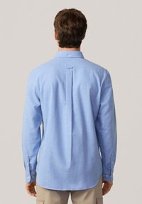 Camisa azul claro de botones con collar, mangas largas, pliegue en la espalda y dobladillo redondeado. Hecha de una tela texturizada, presenta puños abotonados.