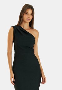 Vestido negro de un solo hombro con una silueta ajustada, detalles drapeados y textura suave. El tejido parece elástico y ceñido al cuerpo.