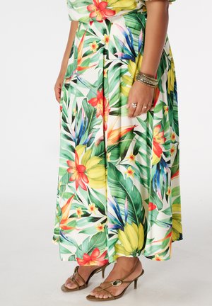Vrouw draagt een kleurrijke maxi-rok met tropische print, een gouden armband, ringen en bruine sandalen met hak en bandjes.