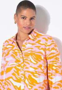 Chemise à boutons avec un motif de rayures de tigre rose et orange ; elle présente un col et une poche avant ; fabriquée en tissu léger.