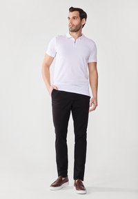 Vit zip-polo t-shirt parat med svarta slim-fit byxor och bruna slip-on skor. Materialen verkar släta och välsittande.