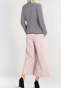 Haut à manches longues rayé noir et blanc associé à un pantalon large rose clair. Le mannequin porte des chaussures noires à talons, tourné de dos à la caméra.