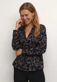 Marineblouse met een bloemenpatroon in beige. Heeft een gedeeltelijke knoopsluiting, lange mouwen en een relaxte pasvorm met een ronde zoom.