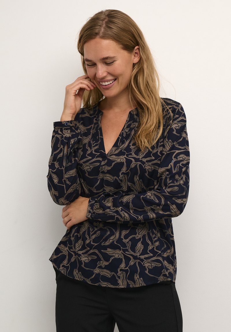 Marineblouse met een bloemenpatroon in beige. Heeft een gedeeltelijke knoopsluiting, lange mouwen en een relaxte pasvorm met een ronde zoom.