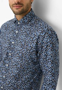 Hemd mit Knopfleiste und abstraktem Muster in Blau, Schwarz und Weiß, mit einem Standardkragen und weißen Knöpfen auf der Knopfleiste.