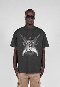 Grå t-shirt lavet af bomuld med et grafisk tryk af en englefigur med vinger og stiliseret tekst foran.