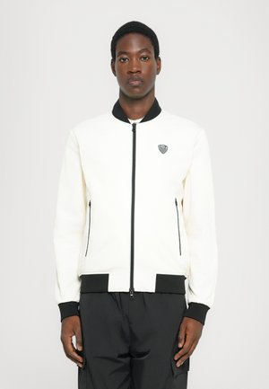 White bomber jacket with black collar and cuffs; features zippered side pockets and a small logo on the left chest; smooth texture.