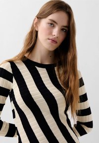 Stribet sweater med smalle sorte og cremefarvede lodrette striber, ribbet tekstur, rund halsudskæring og lange ærmer.
