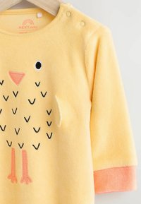 Gelbes Fleece-Babysweatshirt mit besticktem Kükenmotiv, ausgestattet mit schwarzen und rosa Details, Druckknopf-Verschlüssen an den Schultern und orangen Bündchen.