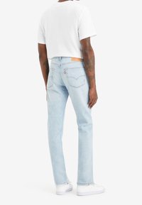 Ljusblå denimjeans med rak benpassform, med subtil blekning, bakfickor och en tanlätt läderetikett vid midjan. Bärs med en vit t-shirt.