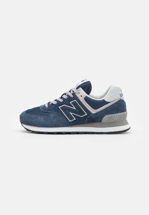 Zapatilla deportiva New Balance azul y gris con materiales de ante y malla, cordones blancos y suela acolchada blanca y gris.