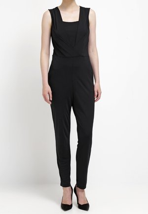 Combinaison noire avec un décolleté carrée, sans manches et jambes fuselées. Fabriquée dans un tissu lisse, elle présente une taille cintrée et des accents minimaux.