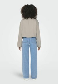 Ljust grå långärmad skjorta med avslappnad passform, ihopsatt med högmidjade blå vida jeans och vita sneakers, sedd bakifrån.