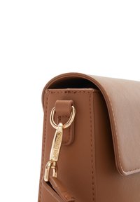 Sac à main brun texturé avec une forme structurée, doté d'un fermoir en métal doré et d'un pendentif logo accroché sur le côté.