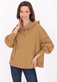 Beige, oversized Kapuzen-Sweatshirt mit Reißverschluss vorne, großer Fronttasche und gerippten Bündchen. Aus weichem Stoff mit lockerer Passform und Kapuzendetail.
