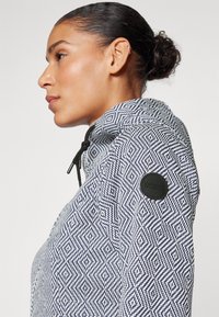 Giacca a zip con motivo navy e bianco, con colletto rialzato, dotata di una patch con logo nero sulla manica e cordoncino regolabile.