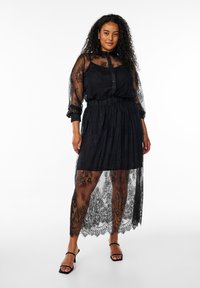 Black lace dress featuring a sheer overlay, buttoned front, and elastic waist. Long sleeves with floral patterns and scalloped hem.