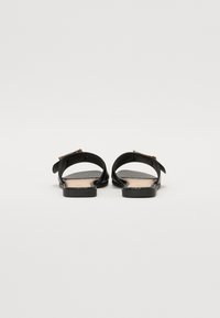 Sandales plates noires avec une sangle réglable, semelle intérieure texturée et semelles lisses. Présente un accent métallique sur la sangle.