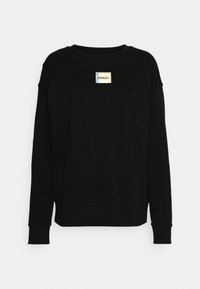 Sudadera negra de manga larga. Presenta un parche rectangular con el logotipo "HUGO" en el centro. Diseño simple con puños de canalé.