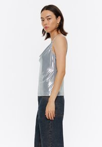 Top de tanque metálico plateado con un frente drapeado, tirantes finos y una silueta ajustada, combinado con jeans de mezclilla oscura de talle alto.