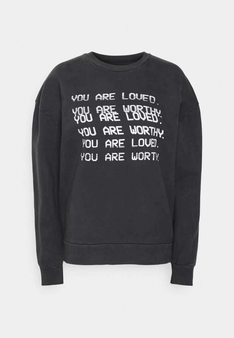 Svart sweatshirt med vit text: "DU ÄR ÄLSKAD" och "DU ÄR VÄRD," i varierande storlekar och orienteringar. Ribbad mudd och halsringning.